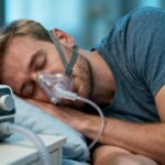 Personne caucasienne dormant paisiblement avec une machine cpap sur la table de nuit, éclairée par une lumière naturelle douce